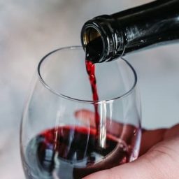 A glass of red wine being poured from a bottle.
