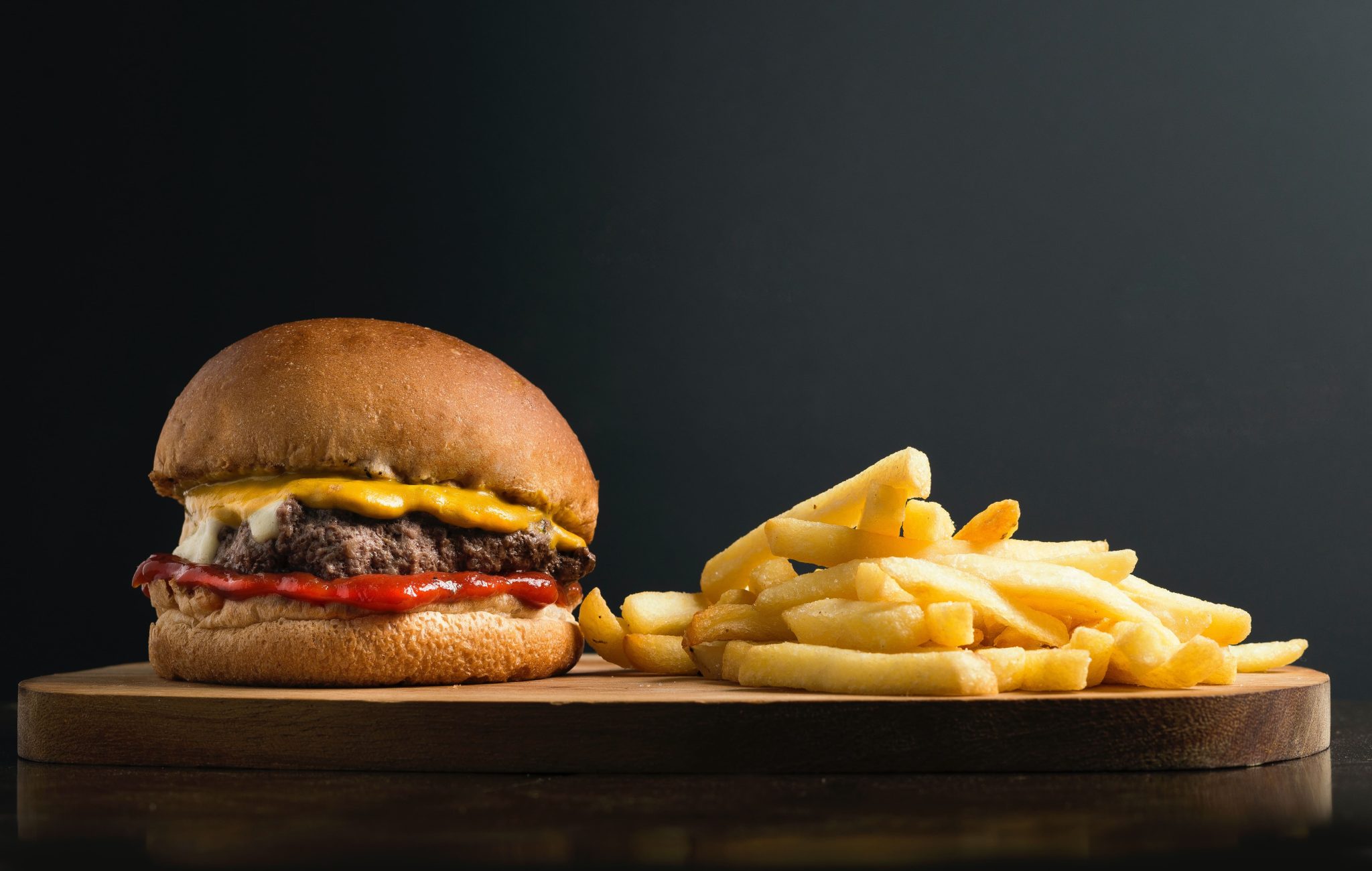 Picture of a cheeseburger and fries against a black background.