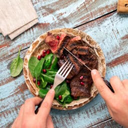 Man eats steak and spinach on a wooden table.