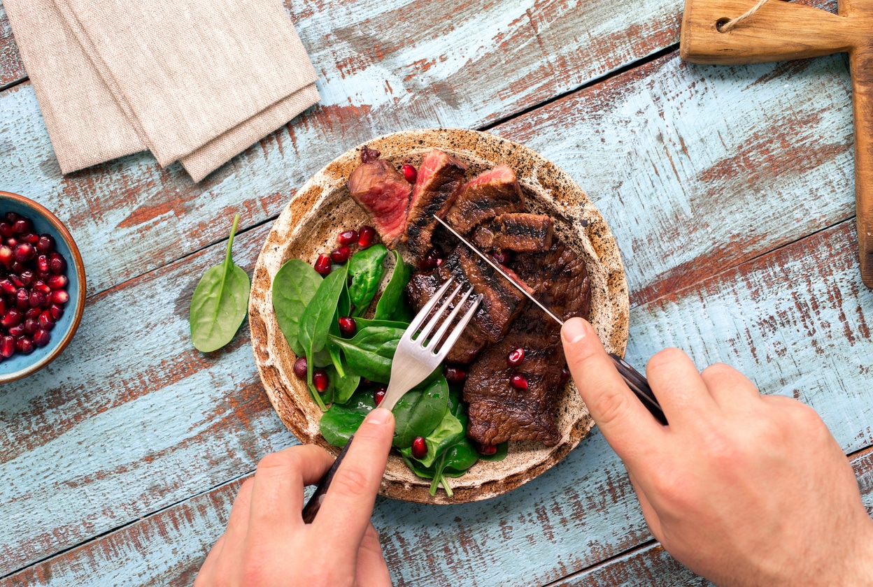 Man eats steak and spinach on a wooden table.